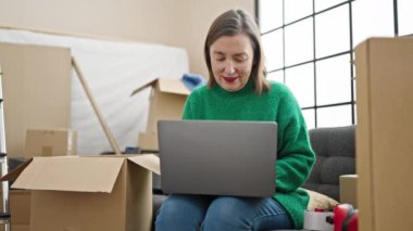 Yeni evindeki koltukta oturan, laptopunu kullanan, gri saçlı, olgun İspanyol bir kadın.