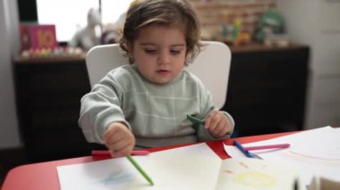 Anaokulunda masaya oturmuş kağıda resim çizen sevimli İspanyol kız öğrenci.