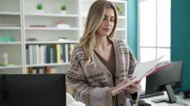 Young blonde woman teacher reading book doing silence gesture at library university