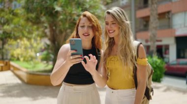 Two women standing together using smartphone at park