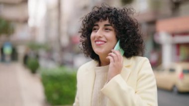 Gülümseyen genç bir kadın caddedeki akıllı telefondan konuşuyor.