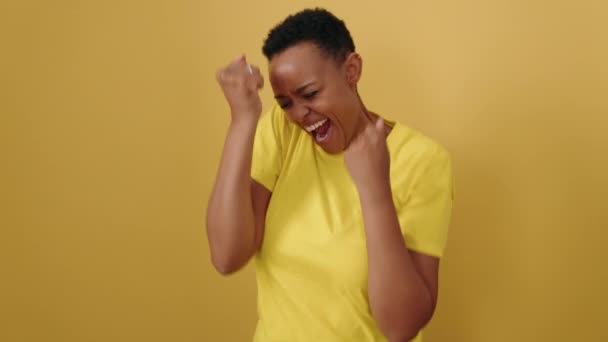 アフリカ系アメリカ人女性の笑顔自信を持って行う勝者式上の孤立した黄色の背景 — ストック動画