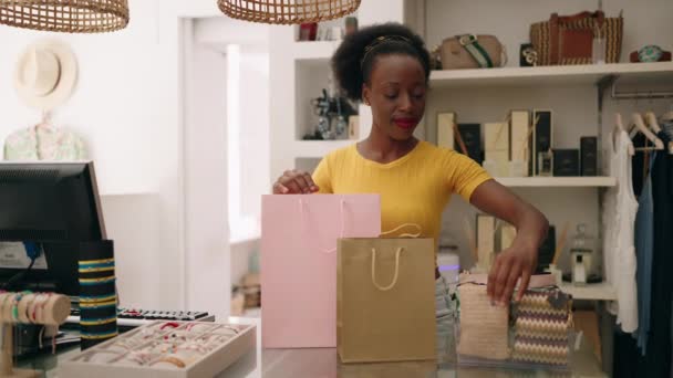 アフリカ系アメリカ人女性ショップアシスタントが衣料品店で買い物袋を準備 — ストック動画