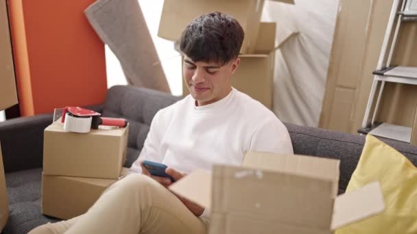 Hombre Hispano Joven Usando Teléfono Inteligente Sentado Sofá Nuevo Hogar — Vídeo de stock