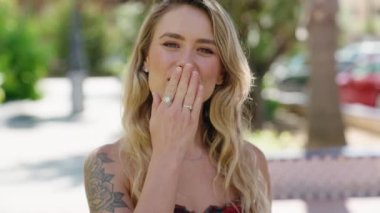 Genç sarışın kadın gülümsüyor. Parkta el ele öpüşme hareketi yapıyor.