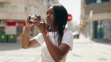 Genç Afrikalı Amerikalı kadın caddede klasik kamera kullanıyor.