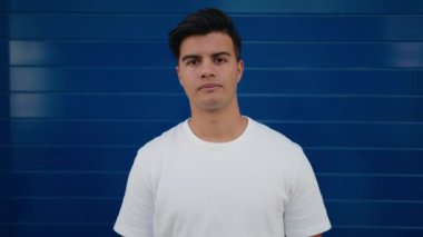 İzole edilmiş mavi arka planda duran kendine güvenen İspanyol genç adam.