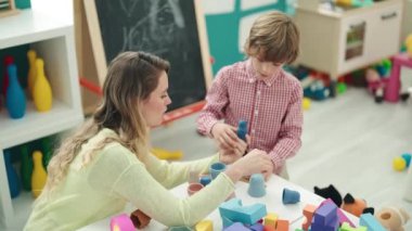 Teacher and toddler playing with toys sitting on table at kindergarten