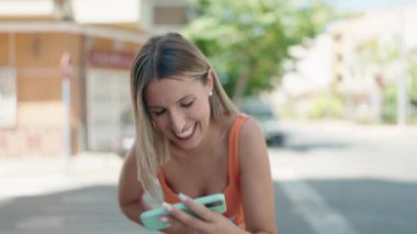 Genç ve güzel İspanyol kadın gülümsüyor. Sokakta akıllı telefondan videolar izliyor.