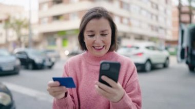Sokakta akıllı telefon ve kredi kartı kullanan orta yaşlı bir kadın.