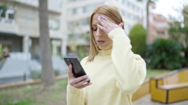 Parkta akıllı telefon kullanan genç sarışın kadın.