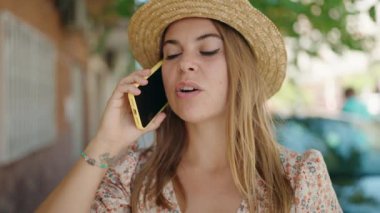 Young woman tourist wearing summer hat talking on smartphone at street