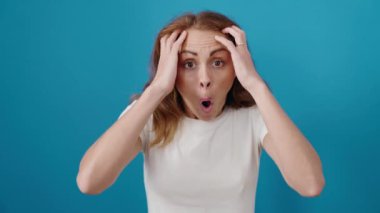 İzole edilmiş mavi arka planda sürpriz bir ifadeyle duran genç, güzel İspanyol kadın.