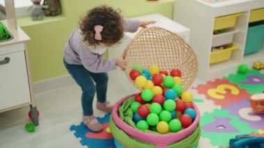 Adorable hispanic girl playing with balls standing at kindergarten