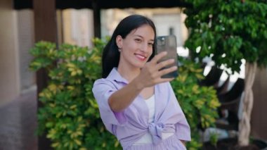 Genç ve güzel İspanyol kadın gülümsüyor. Kendine güveni tam. Sokakta akıllı telefonun yanında selfie çekiyor.