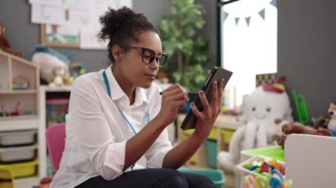 African american woman preschool teacher using touchpad sitting on chair at kindergarten