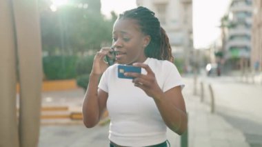 Afro-Amerikalı kadın akıllı telefondan konuşuyor ve parkta kredi kartı kullanıyor.