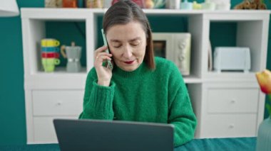 Erişkin İspanyol kadın, gri saçlı, yemek odasında dizüstü bilgisayar kullanıyor.