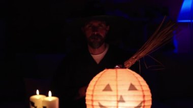 Büyücü kostümü giymiş genç kel adam elinde süpürge tutuyor.