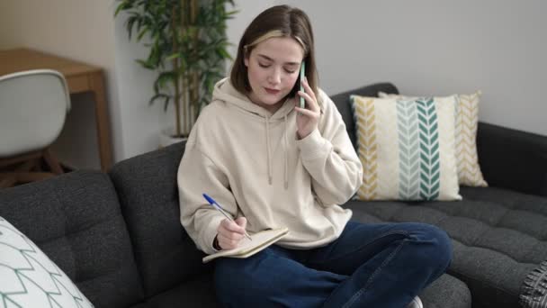 Young Blonde Woman Writing Notebook Talking Smartphone Home — Stockvideo