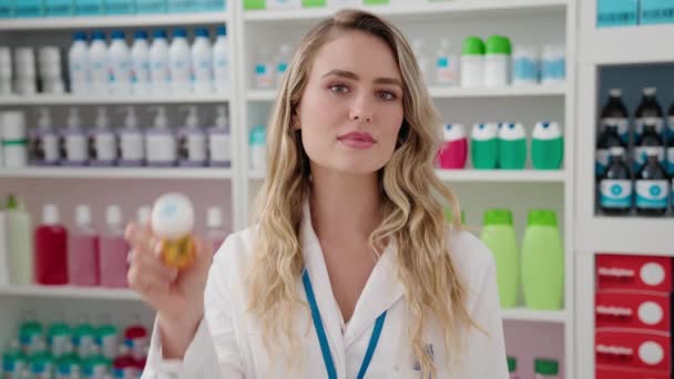 Young Blonde Woman Pharmacist Smiling Confident Holding Pills Bottle Pharmacy — kuvapankkivideo