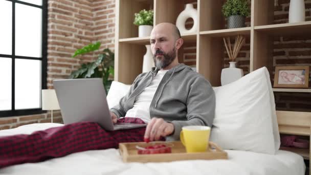 Genç Kel Adam Kahvaltısını Yatak Odasında Dizüstü Bilgisayar Kullanarak Yapıyor — Stok video