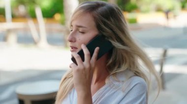 Genç sarışın kadın gülümsüyor. Kendine güveni tam. Akıllı telefondan konuşuyor.