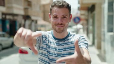 Young hispanic man smiling confident doing photo gesture with hands at street