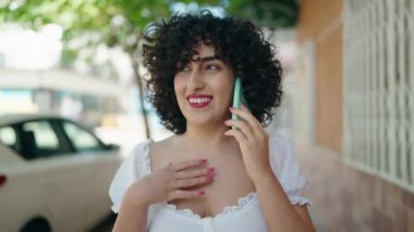 Orta Doğulu genç bir kadın sokakta akıllı telefondan konuşuyor.