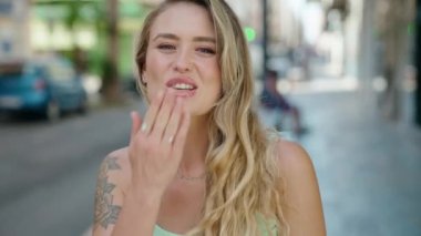Genç sarışın kadın gülümsüyor. Kendine güveniyor. Öpüşme hareketi yapıyor.