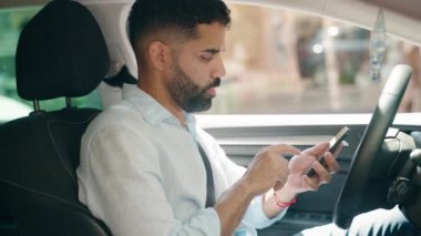 Young arab man using smartphone sitting on car at street