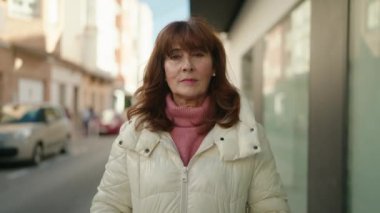 Orta yaşlı, yüzü rahat bir şekilde caddede duran kızıl saçlı kadın.
