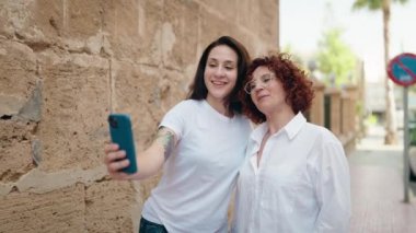 İki kadın anne ve kız sokakta akıllı telefonla selfie çekiyorlar.