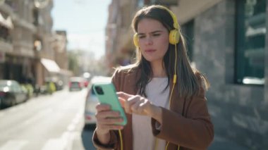 Beyaz kadın gülümsüyor. Kendine güvenen, müzik dinleyen caddede akıllı telefon kullanan.