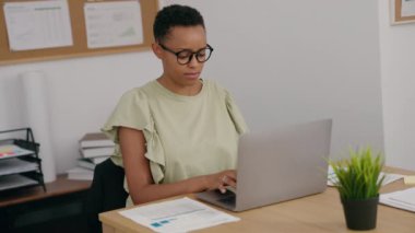 Afrika kökenli Amerikalı iş kadını laptopunu ofiste elleri rahat olarak kullanıyor.