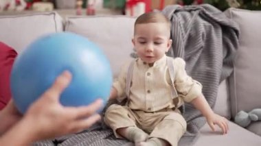 Öğretmen ve anaokulu öğrencisi evdeki Noel ağacının yanında kanepede top oynuyorlar.