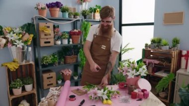 Young redhead man florist make bouquet of flowers at flower shop