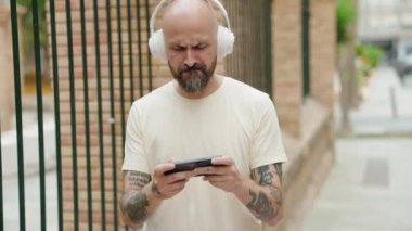 Genç kel adam gülerek sokakta video oyunu oynuyor.