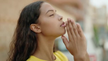 Young african american woman praying with closed eyes at street