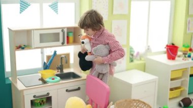 Anaokulunda oyuncak bebekleri tutan sevimli beyaz çocuk.