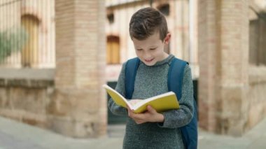 Blond child student hugging book standing at street