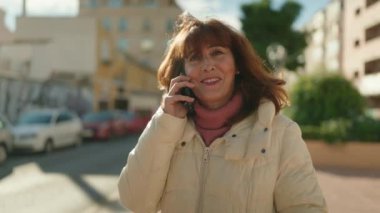 Middle age redhead woman smiling confident talking on the smartphone at street