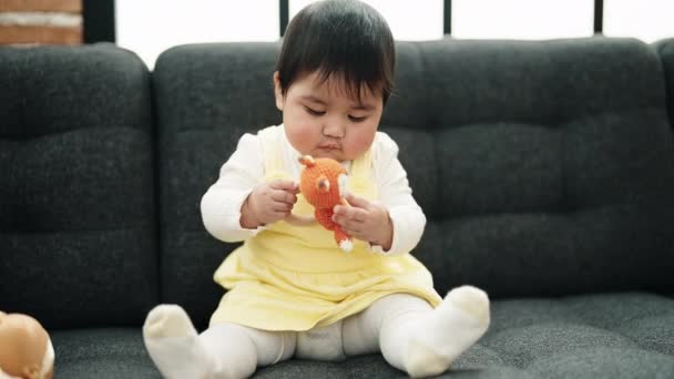 Adorable Hispanic Baby Holding Toy Sitting Sofa Home — Stockvideo