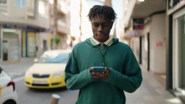Sokakta akıllı telefon kullanan, kendinden emin gülümseyen Afrikalı Amerikalı bir adam.