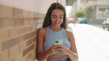 Genç, güzel, İspanyol bir kadın sokakta akıllı telefon kullanarak gülümsüyor.