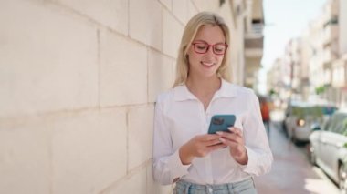 Sokakta akıllı telefon kullanan, kendine güvenen genç sarışın kadın.