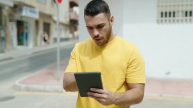 Latin kökenli genç bir adam sokakta ciddi bir ifadeyle dokunmatik ped kullanıyor.