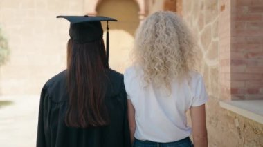 Two women mother and graduated daughter standing with arms crossed gesture at campus university
