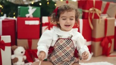 Sevimli İspanyol kız evdeki Noel ağacının yanında yerde oturmuş çember oyuncağıyla oynuyor.