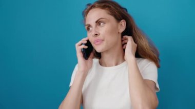 Genç, güzel, İspanyol bir kadın gülümsüyor. Akıllı telefondan kendine güvenen, izole mavi arka planda konuşan.